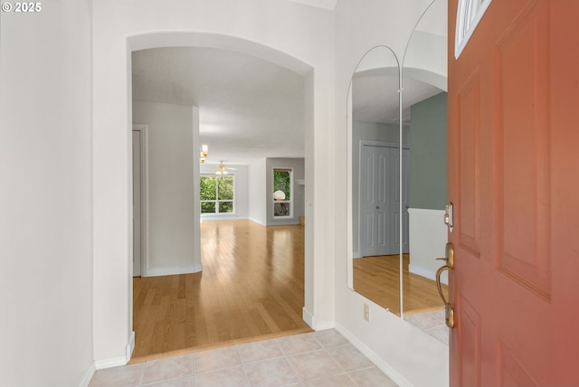foyer with light wood-style flooring, arched walkways, baseboards, and a ceiling fan