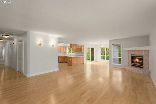 unfurnished living room featuring baseboards, light wood finished floors, visible vents, a sink, and a fireplace