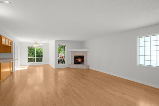 unfurnished living room with a tile fireplace, light wood-style floors, baseboards, and a ceiling fan