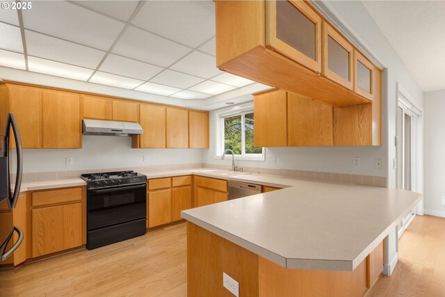 kitchen featuring a sink, a peninsula, black appliances, under cabinet range hood, and light wood-style flooring