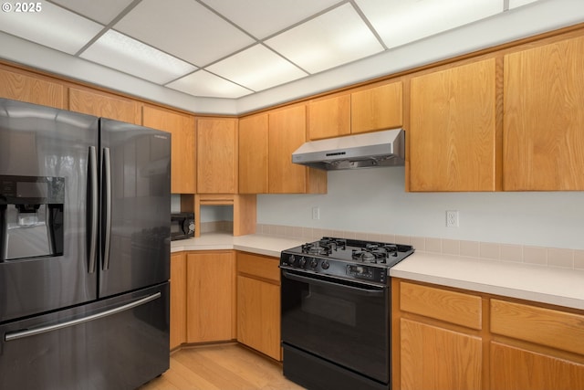 kitchen featuring under cabinet range hood, light countertops, black gas range oven, and stainless steel fridge