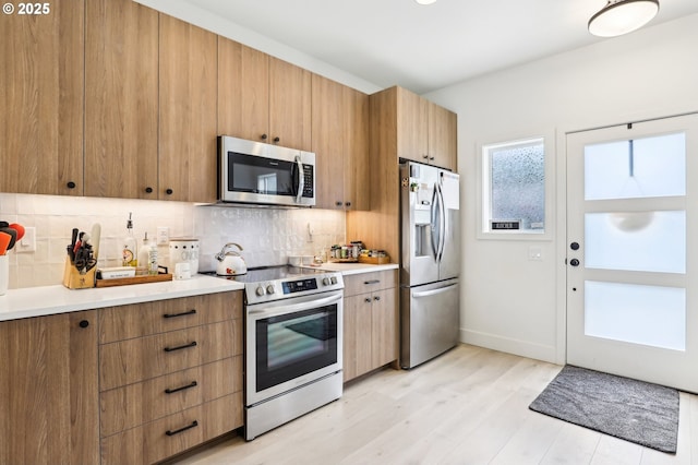 kitchen with light countertops, decorative backsplash, stainless steel appliances, and light wood finished floors