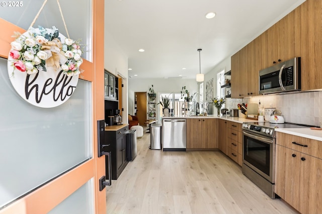 kitchen with light wood-style floors, light countertops, stainless steel appliances, a peninsula, and decorative backsplash