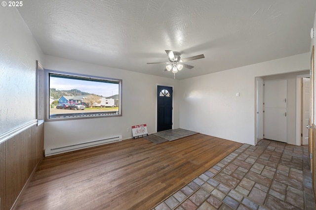 interior space with a textured ceiling, a baseboard radiator, wooden walls, ceiling fan, and hardwood / wood-style floors