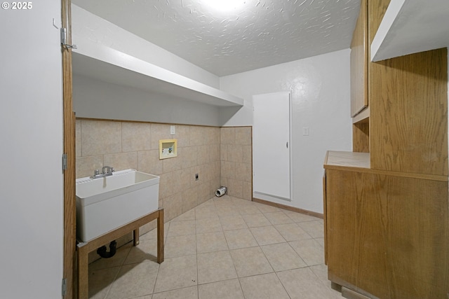 clothes washing area with hookup for a washing machine, light tile patterned floors, a textured ceiling, and tile walls