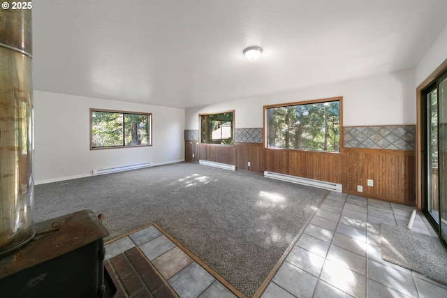 unfurnished living room with wooden walls, light colored carpet, and baseboard heating