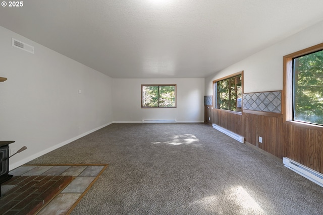 carpeted spare room with a wood stove, baseboard heating, and wood walls