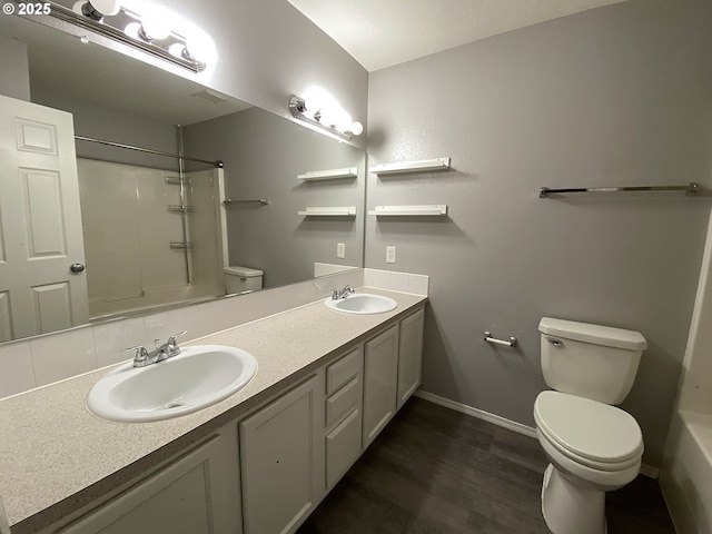 full bath with double vanity, wood finished floors, a sink, and toilet