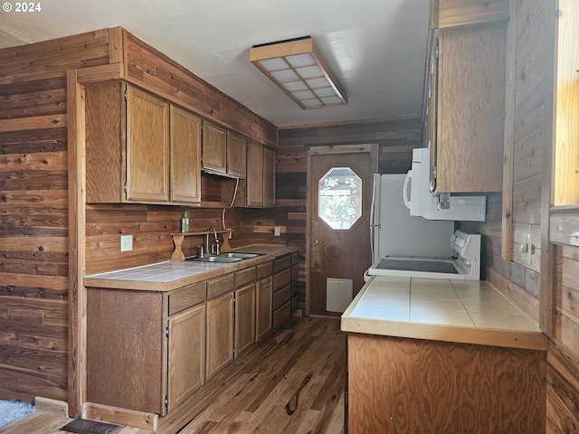 kitchen with electric range, wood walls, dark wood-style flooring, a sink, and tile counters