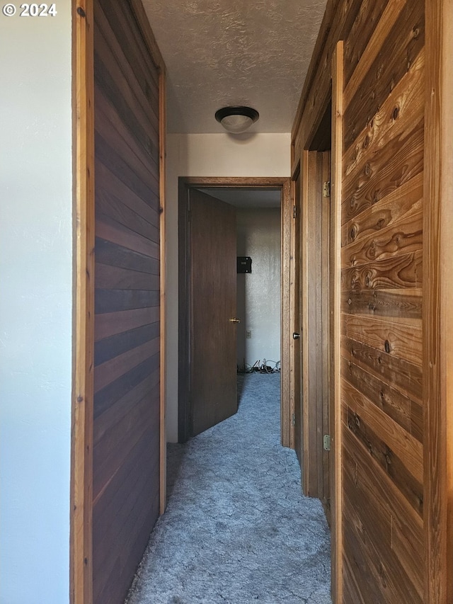 corridor featuring a textured ceiling, carpet flooring, and wooden walls