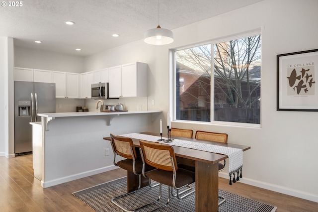 dining area featuring a textured ceiling, baseboards, wood finished floors, and recessed lighting