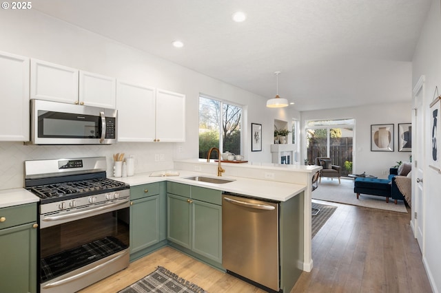 kitchen with a peninsula, green cabinets, stainless steel appliances, and a sink