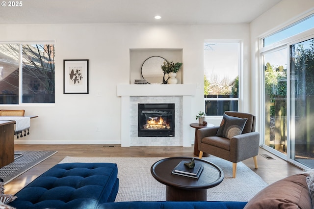 living room featuring baseboards, visible vents, a tiled fireplace, wood finished floors, and recessed lighting