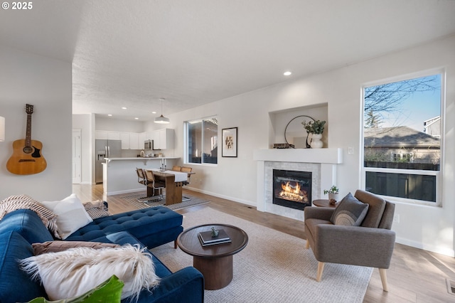 living room featuring baseboards, recessed lighting, a fireplace, and light wood-style floors