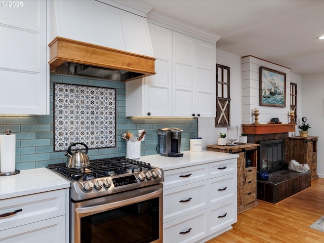 18495 Terry Ave, Lake Oswego, OR 97035 - kitchen with light wood-style floors, stainless steel gas range oven, white cabinetry, custom range hood, and backsplash