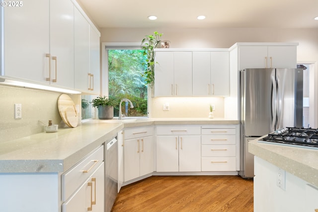 kitchen with stainless steel appliances, a sink, light wood-style flooring, white cabinets, and recessed lighting