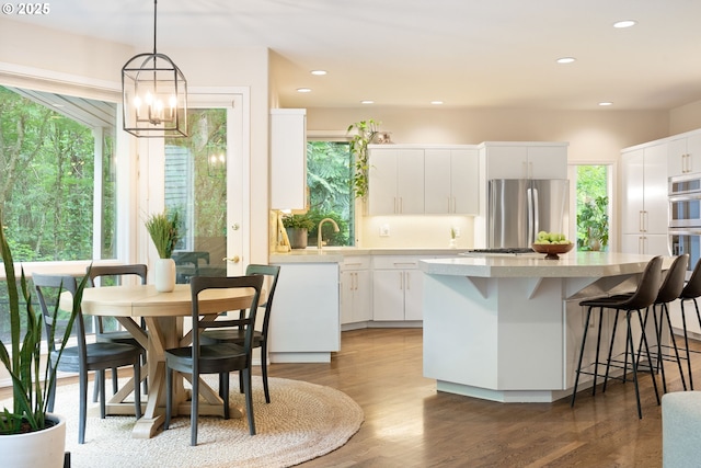 kitchen with stainless steel appliances, a kitchen island, light countertops, wood finished floors, and white cabinetry