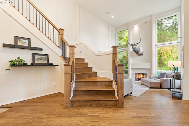stairway featuring a high ceiling, wood finished floors, healthy amount of natural light, a lit fireplace, and baseboards