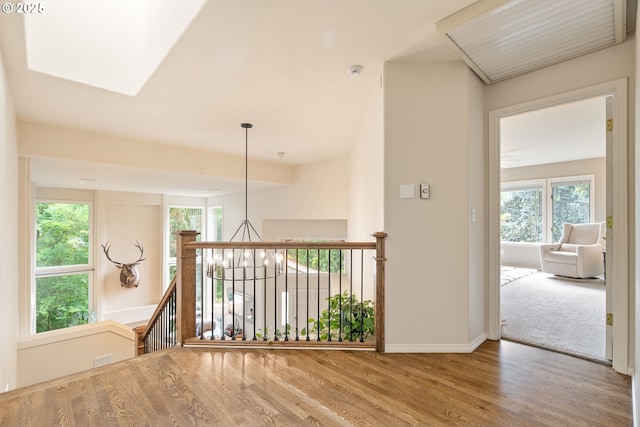 hall with wood finished floors, plenty of natural light, baseboards, and an upstairs landing