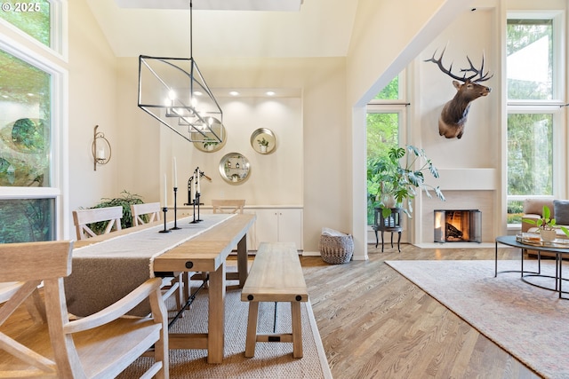 9030 SW Lancelot Ln, Portland, OR 97219 - dining area featuring wood finished floors, a chandelier, high vaulted ceiling, a fireplace with flush hearth, and baseboards