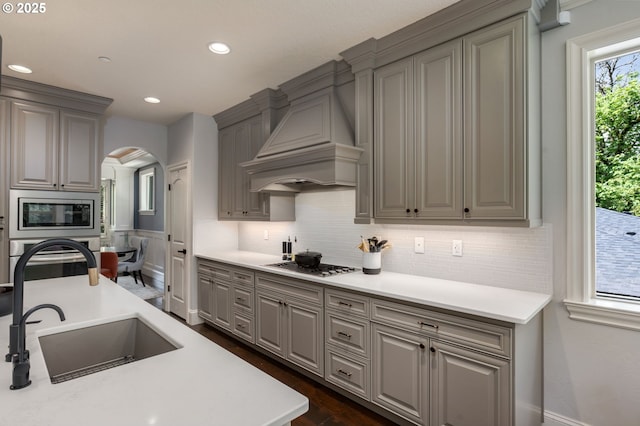 kitchen featuring decorative backsplash, premium range hood, arched walkways, a sink, and stainless steel appliances