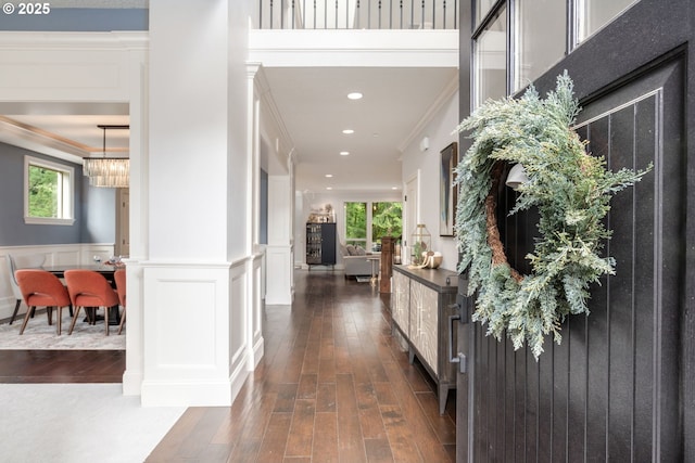 hallway with crown molding, a decorative wall, recessed lighting, a wainscoted wall, and dark wood finished floors