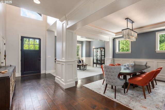 dining space featuring crown molding, ornate columns, wainscoting, and dark wood-type flooring