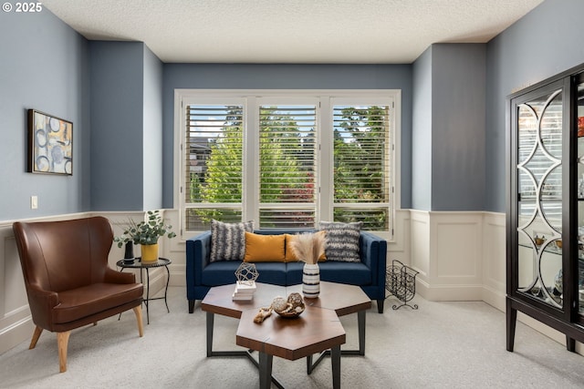 living area featuring a decorative wall, a textured ceiling, light carpet, and a wainscoted wall