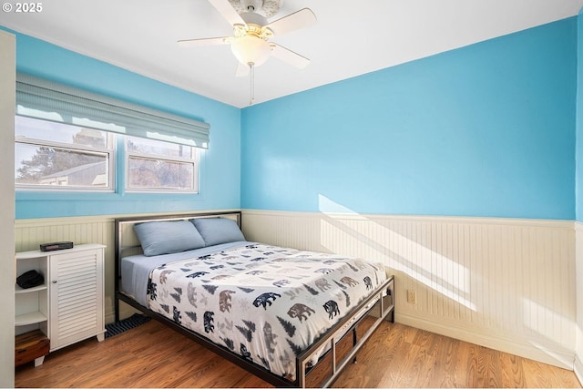 bedroom with a wainscoted wall, ceiling fan, and wood finished floors