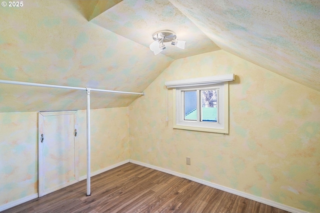 additional living space with vaulted ceiling, a textured ceiling, baseboards, and wood finished floors