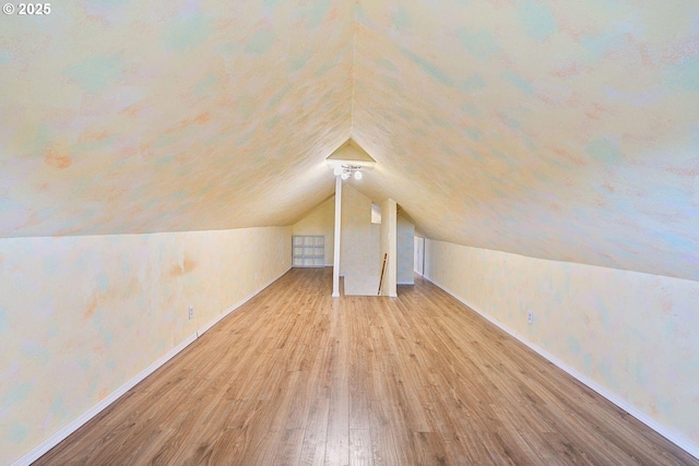 additional living space featuring vaulted ceiling, light wood-type flooring, and baseboards