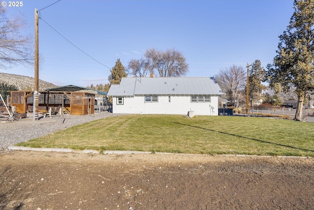 back of house featuring metal roof, a lawn, and stucco siding