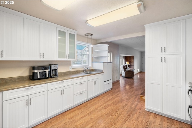 kitchen with light wood finished floors, white cabinets, glass insert cabinets, decorative light fixtures, and a sink