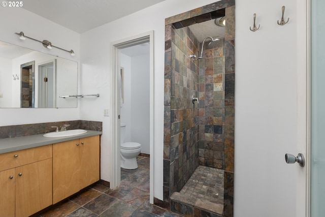 bathroom featuring vanity, a tile shower, and toilet