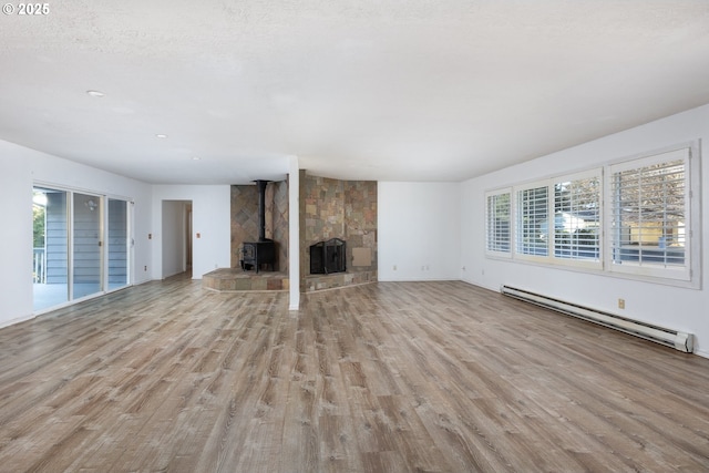 unfurnished living room featuring a healthy amount of sunlight, light wood-type flooring, and a baseboard heating unit