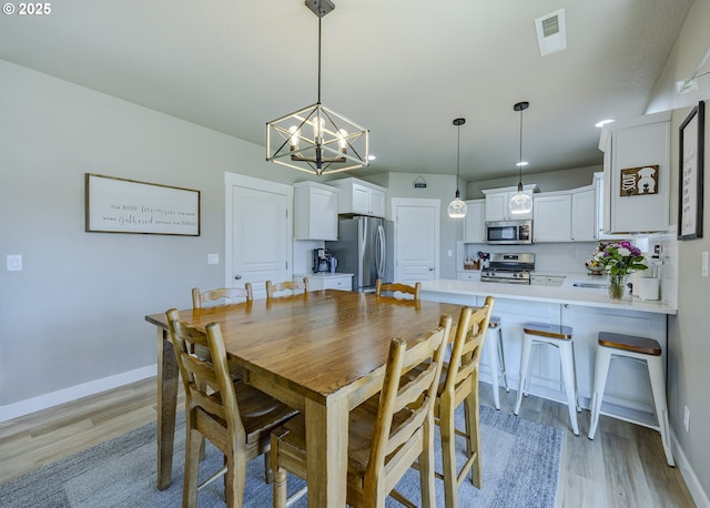 dining area with visible vents, light wood finished floors, baseboards, and an inviting chandelier