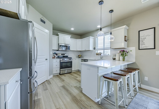 kitchen featuring tasteful backsplash, a peninsula, stainless steel appliances, white cabinetry, and a sink