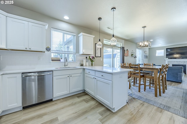 kitchen with light countertops, visible vents, a sink, dishwasher, and a peninsula