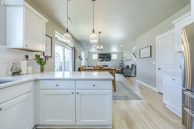 kitchen featuring light wood finished floors, open floor plan, freestanding refrigerator, a peninsula, and white cabinetry