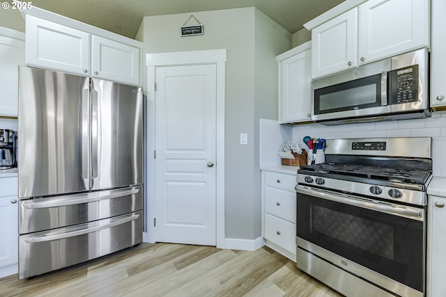 kitchen featuring white cabinetry, light countertops, appliances with stainless steel finishes, backsplash, and light wood finished floors