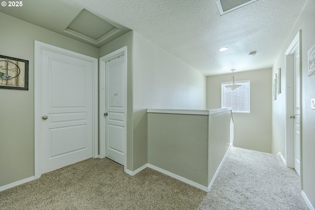 hall featuring a textured ceiling, carpet floors, visible vents, an upstairs landing, and attic access