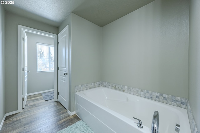 full bathroom with wood finished floors, a textured ceiling, baseboards, and a bath