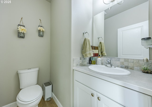 half bathroom featuring toilet, wood finished floors, vanity, baseboards, and backsplash