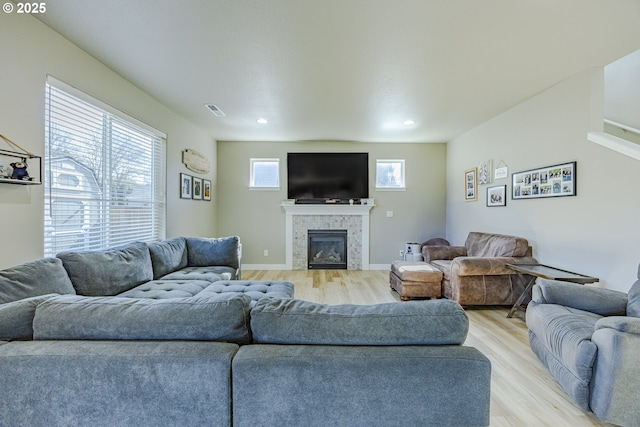 living room with a tile fireplace, visible vents, light wood-style flooring, and baseboards