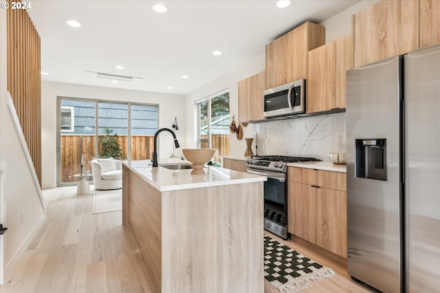 kitchen with modern cabinets, an island with sink, a sink, appliances with stainless steel finishes, and light countertops