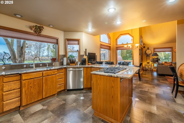 kitchen featuring a peninsula, appliances with stainless steel finishes, a sink, light stone counters, and brown cabinetry