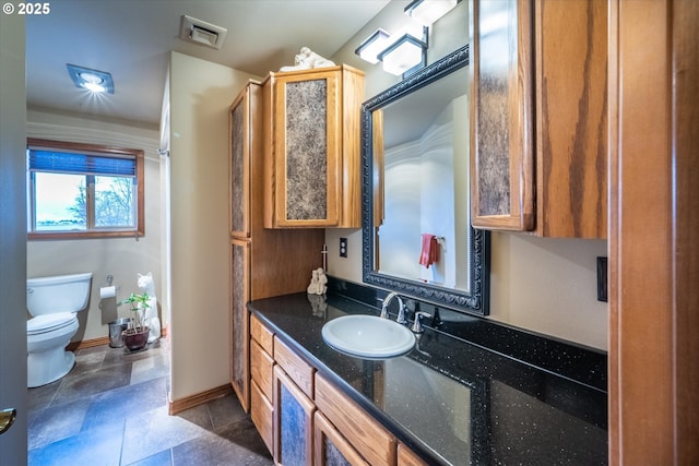 bathroom featuring visible vents, stone finish floor, baseboards, toilet, and vanity