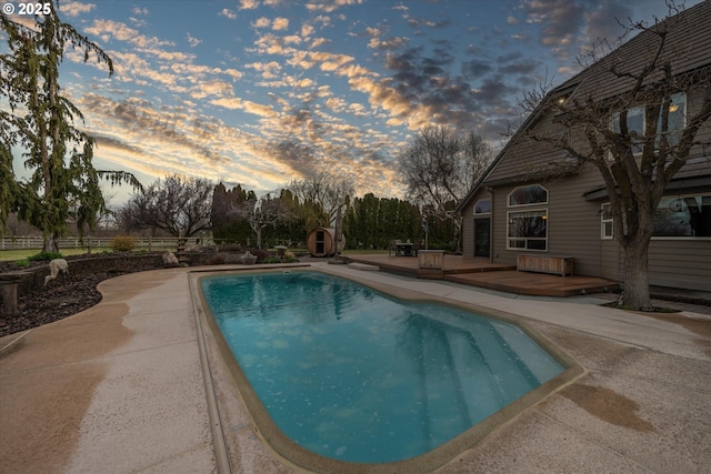 pool at dusk featuring a patio, fence, a wooden deck, and an outdoor pool