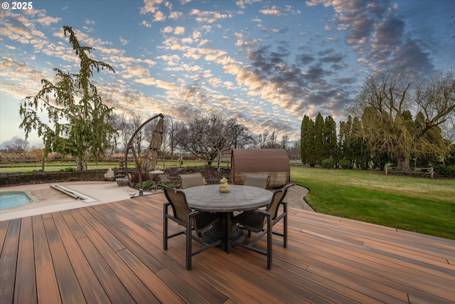 deck at dusk featuring outdoor dining area and a yard