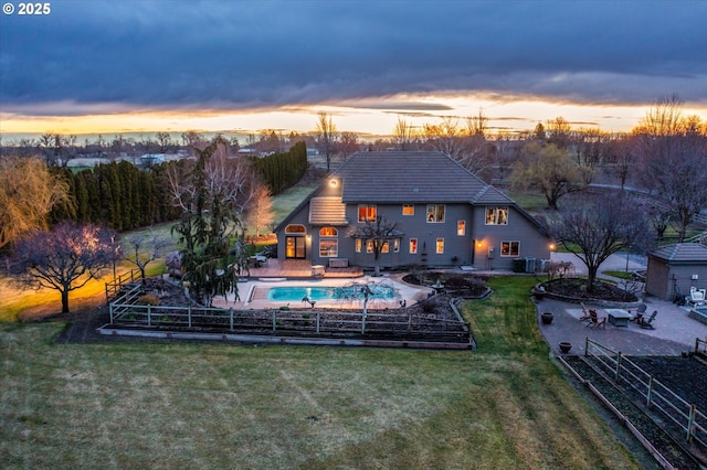back of house at dusk with fence, a patio, a fenced in pool, a tile roof, and a yard